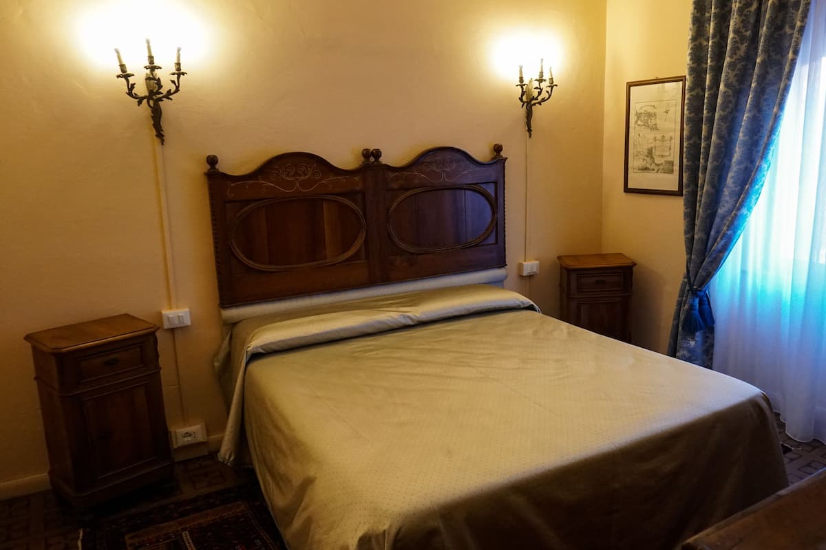 A neatly made bed in a room with a wooden headboard, two bedside tables, and a wall-mounted light fixture.