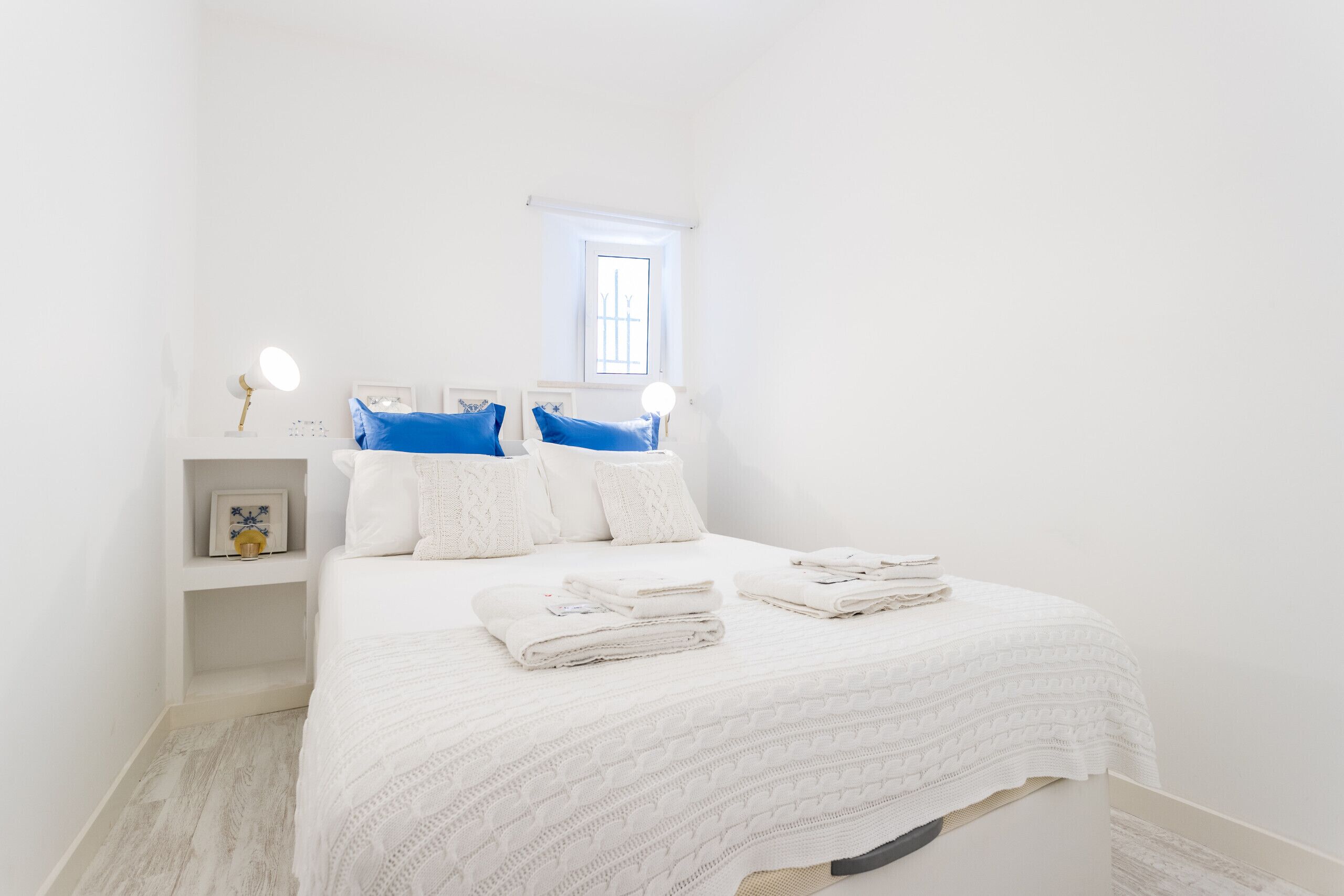 A neatly arranged bedroom with a bed, pillows, a bedside table, and a window.