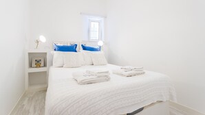 Quarto bem arrumado com cama, travesseiros, mesa de cabeceira e janela.