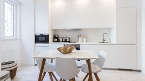 Cozinha moderna com armários brancos, uma mesa de jantar com cadeiras e uma janela grande.