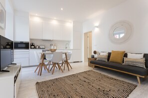 Eine moderne Küche mit weißen Schränken, ein Essbereich mit Tisch und Stühlen sowie ein Wohnbereich mit einer Couch und einem runden Spiegel an der Wand.