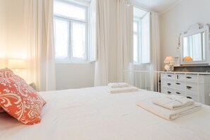 A bedroom with a bed, pillows, a dresser, a mirror, and a window with curtains.