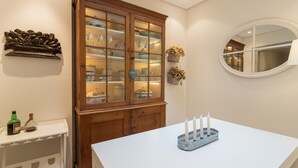 Une pièce comprenant une table blanche, un meuble en bois doté de portes en verre, un miroir et une étagère ornée d’objets décoratifs.