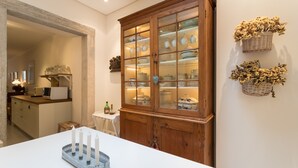 Une cuisine avec un meuble en bois où sont exposées de la vaisselle, une table blanche décorée de bougies et un panier mural contenant des fleurs séchées.