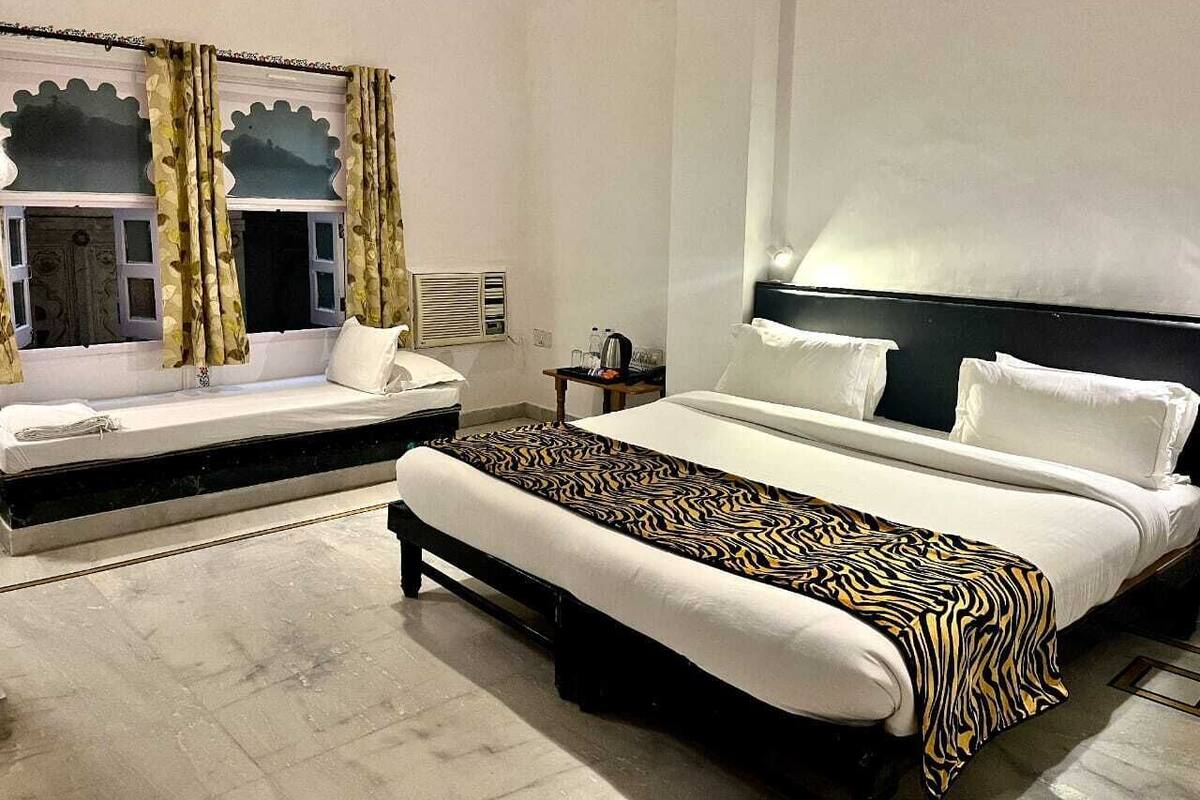 Een slaapkamer met een bed, een slaapbank, een bankje, een nachtkastje en een wandplank.
