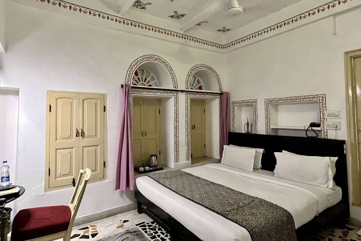 Een slaapkamer met een bed, een stoel, een garderobe en een spiegel.