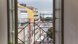 Une vue à travers une fenêtre sur un paysage urbain, avec des bâtiments et une étendue d’eau au loin.