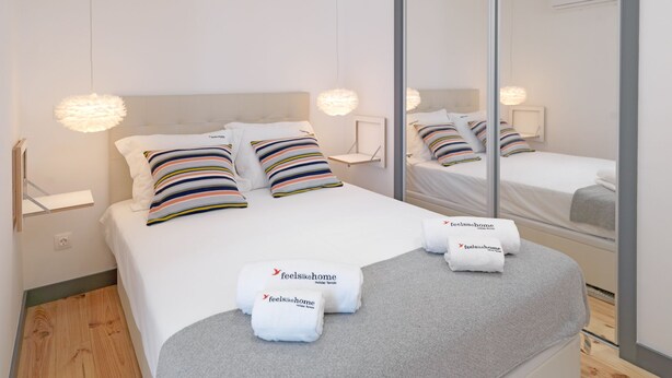 A modern hotel room with a large bed, striped pillows, a mirror, and two towels with the hotel's branding.