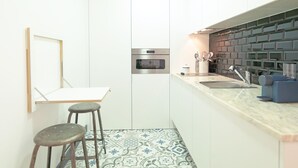A compact kitchen with white cabinets, a built-in oven, a sink, and a patterned backsplash.
