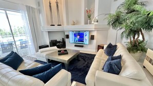 Een moderne woonkamer met een flatscreentelevisie, witte banken, een bijzettafeltje en een grote potplant.