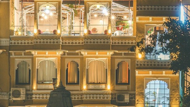 Un edificio de varios pisos con balcones ornamentados, grandes ventanales con cortinas e iluminación decorativa.