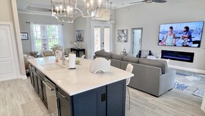 Una cocina moderna con una isla grande, una zona de comedor con sofá y un televisor en la pared.
