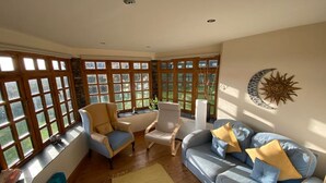 Ein Wintergarten mit großen Fenstern, einem blauen Sofa, zwei Sesseln und einer Wanddekoration mit Sonne und Mond.