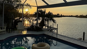 A pool area with two inflatable rings, a covered seating area, and a view of the sunset over water. - TOP FLORIDA's Villa Lake View (Cape Coral)