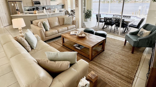 A spacious living room with a large sofa, a coffee table, and a view of a dining area and water through large glass doors. - TOP FLORIDA's Villa Lake View (Cape Coral)