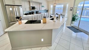 A modern kitchen with a large island, stainless steel appliances, and a view of the ocean through large windows. - TOP FLORIDA's Villa Lake View (Cape Coral)