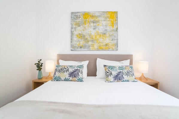 A neatly made bed with white linens, two matching pillows, and a wall-mounted abstract painting.