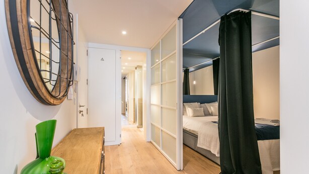 A modern bedroom with a bed, a desk, and a chair. There is a door leading to another room. - FLH Chiado Modern Place (Lisbon)