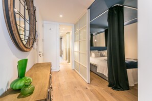 A modern bedroom with a bed, a desk, and a chair. There is a door leading to another room.