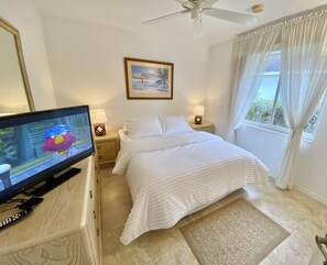 A hotel room with a bed, a television, a ceiling fan, and a window with curtains. - TOP FLORIDA's Villa Parrot Key (Cape Coral)