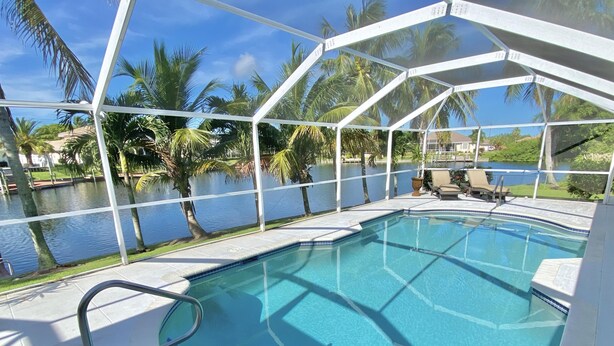 A clear blue pool with a white deck, surrounded by palm trees and a view of a lake. - TOP FLORIDA's Villa Parrot Key (Cape Coral)