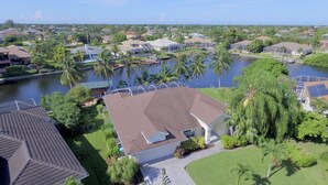 A residential area with houses, a body of water, and a large house with a sloped roof and solar panels. - TOP FLORIDA's Villa Parrot Key (Cape Coral)