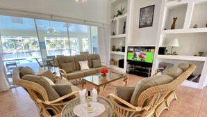 A living room with wicker furniture, a glass coffee table, and a television. - TOP FLORIDA's Villa Parrot Key (Cape Coral)