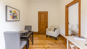 Ein gemütlicher Raum mit Holztür, einem Esstisch mit Stühlen, einem weißen Sofa und einem gerahmten abstrakten Kunstwerk an der Wand.