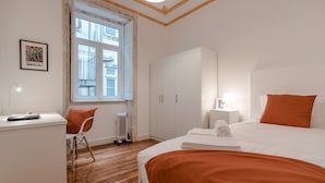 Un dormitorio con cama, escritorio, silla, radiador y ventana.