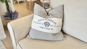 Un sofá color beige con un cojín a rayas que dice "Villa Stardusk, Cape Coral, FL" y coordenadas.