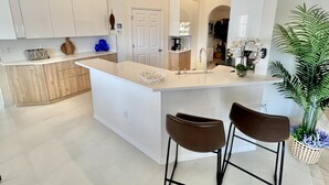 Una cocina moderna con una isla central, taburetes de bar y una planta en maceta.