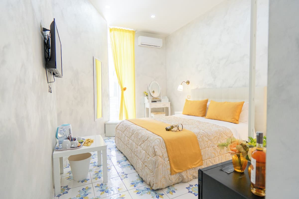 A hotel room with a bed, a desk, a chair, a TV, and an air conditioning unit.