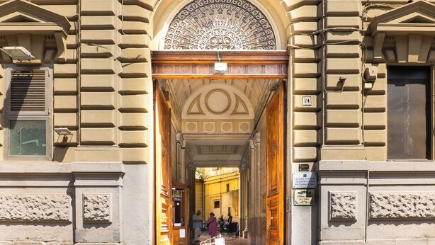 An entrance with a decorative archway, a sign for a college, and a pathway leading into a building. - Alma Adry (Naples)