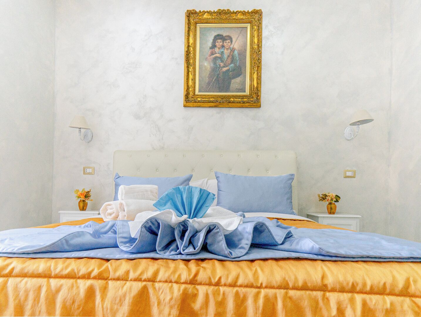 A neatly made bed with a blue and white duvet, a white headboard, and a framed picture on the wall.