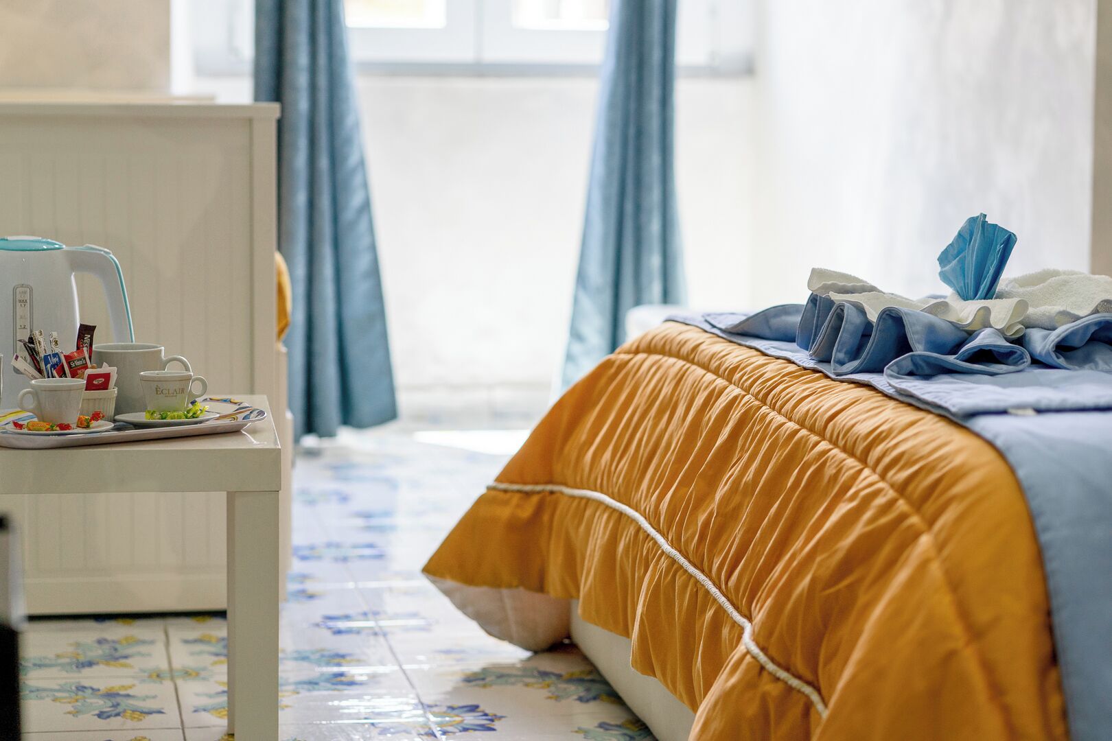 A hotel room with a bed, a bedside table with a coffee maker, and a tray with breakfast items.