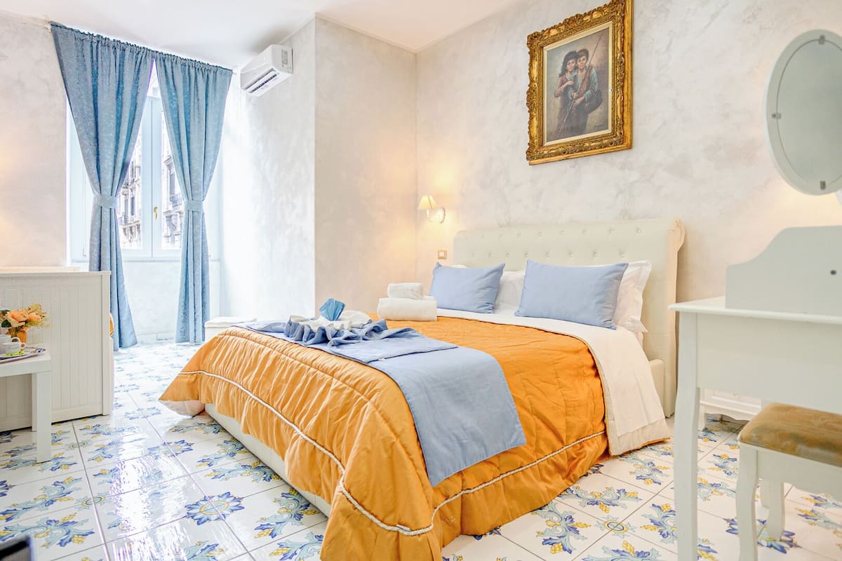 A hotel room with a bed, a bedside table, a chair, a desk, and a window with curtains.