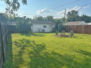 A backyard with a grassy lawn, a wooden fence, and a small house with a chimney.