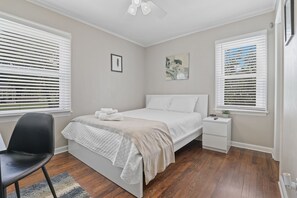A bedroom with a bed, a chair, a nightstand, and a window with blinds.