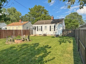 A residential backyard with a wooden fence, a brick fire pit, and a grassy lawn.