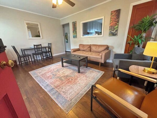 A living room with a sofa, coffee table, and chairs. There is a dining table with chairs, a rug, and a door with a red frame.