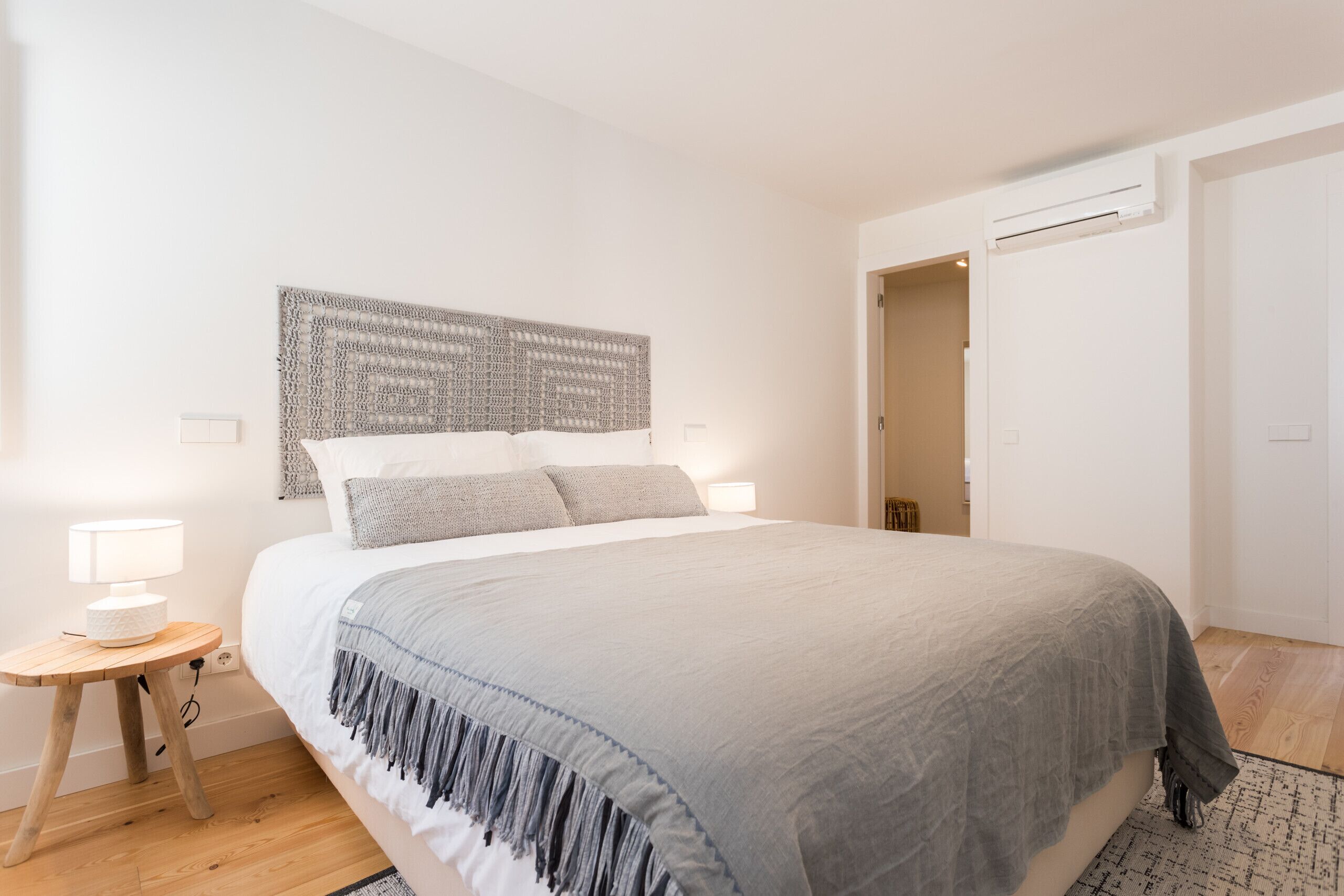 Ein modernes Schlafzimmer mit einem großen Bett, einem Kopfteil mit Strukturmuster, Nachttischlampen und Holzboden.