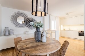 A modern kitchen with white cabinets, a wooden dining table with chairs, and a decorative mirror on the wall.