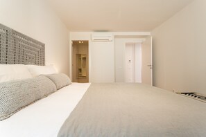 A bedroom with a large bed, a headboard, an air conditioning unit, and a door leading to a bathroom.