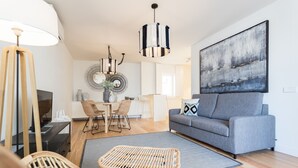 Un salon moderne avec un canapé gris, des fauteuils en osier, une table à manger avec des chaises, une grande peinture abstraite et un luminaire suspendu.