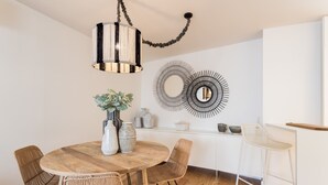 Un coin repas comprenant une table ronde en bois, des chaises en osier, un luminaire suspendu et des œuvres d’art décoratives accrochées au mur.