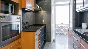 A modern kitchen with wooden cabinets, stainless steel appliances, and a black countertop. - FLH Marquês Trendy Apartment (Lisboa ciudad)
