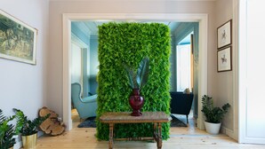 A room with a wooden floor, a green vertical garden wall, a dark blue armchair, and a small table with a vase. - FLH Marquês Trendy Apartment (Lisboa ciudad)