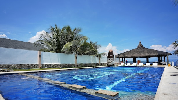 Una piscina con agua azul cristalina, un quiosco con techo de paja y palmeras al fondo.