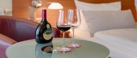 Une chambre d’hôtel avec un lit, une petite table ronde, une bouteille de vin et deux verres.