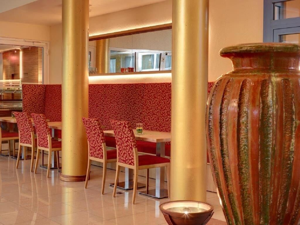 A restaurant with booths and red upholstered chairs, a large vase, and a mirror on the wall.